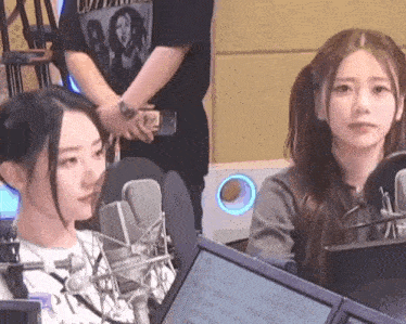 two women are sitting in front of microphones in a room .