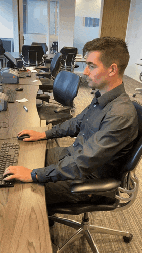 a man in a black shirt sits at a desk using a keyboard and mouse