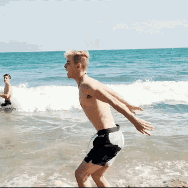 a shirtless man is running into the ocean while another man sits in the water