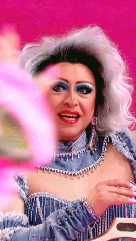 a drag queen is looking at herself in the mirror