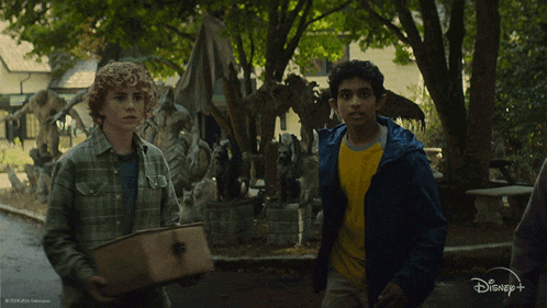 two boys walking in a park with a disney logo in the corner