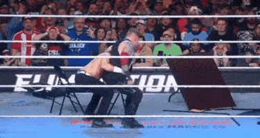two wrestlers are fighting in a wrestling ring with a table in the middle of the ring .