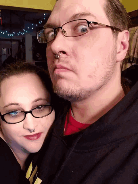 a man with glasses and a nose ring looks at the camera