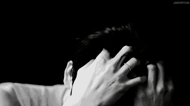 a black and white photo of a person holding their head .