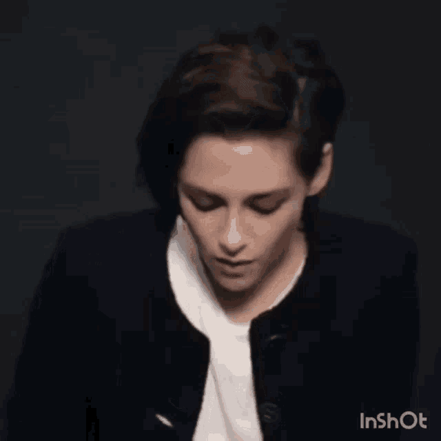 a woman with short hair is wearing a black jacket and white shirt .