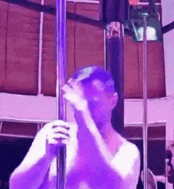 a man without a shirt is standing on a pole in a room with purple lights .