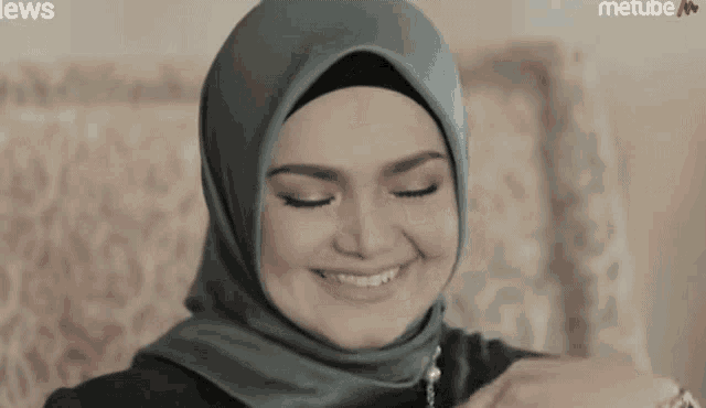 a woman wearing a hijab is smiling in front of a metube logo