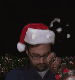 a man wearing a santa hat and glasses is sitting in front of a christmas tree .