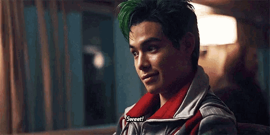 a young man with green hair is sitting down and says sweet