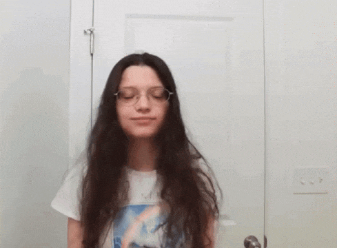 a young girl with long hair and glasses is standing in front of a door .