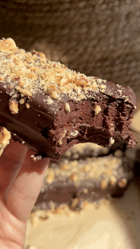 a close up of a person holding a piece of chocolate cake with nuts on top