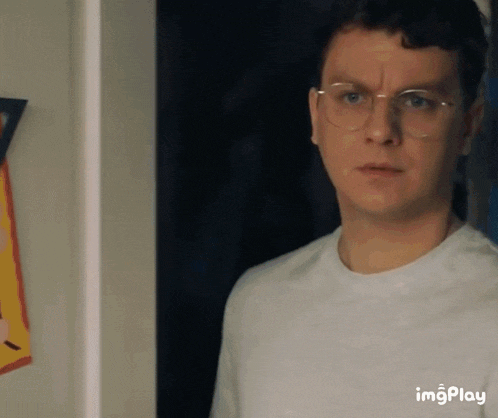 a man wearing glasses and a white shirt is standing next to a wall .