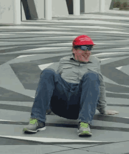 a man wearing a red hat and sunglasses is sitting on a skateboard .