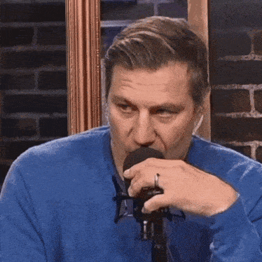 a man wearing a blue sweater and a ring is talking into a microphone