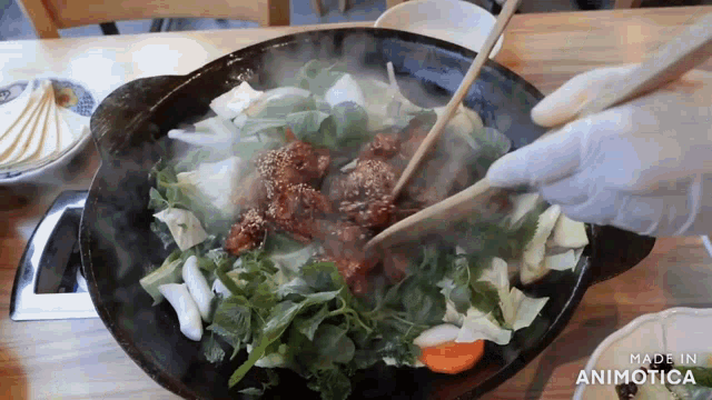 a person is stirring a pot of food with chopsticks and the words made in animotica are visible