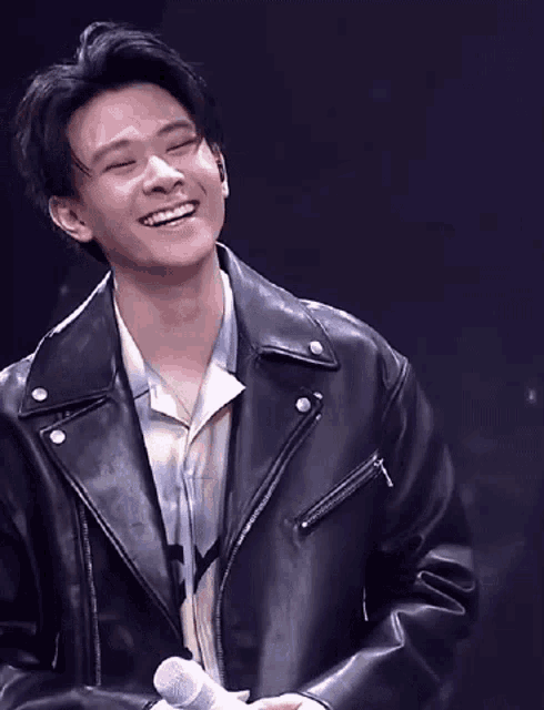 a young man wearing a leather jacket is smiling and holding a microphone .