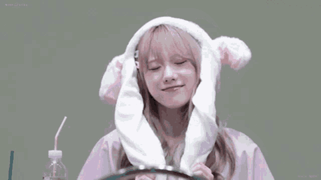 a girl wearing a bunny hat with ears is sitting at a table with a bottle of water .