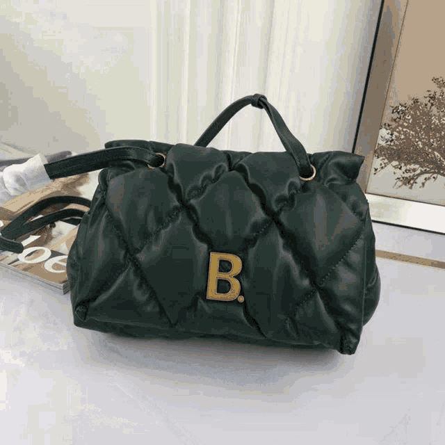 a green quilted purse with a gold letter b on it