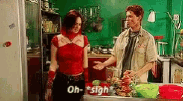 a man and a woman are standing in a kitchen and the woman is saying oh-sigh .