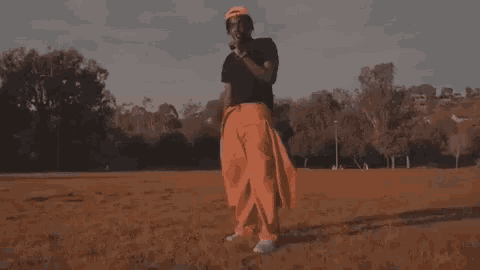 a man in a black shirt and orange pants is standing in a field with trees in the background .