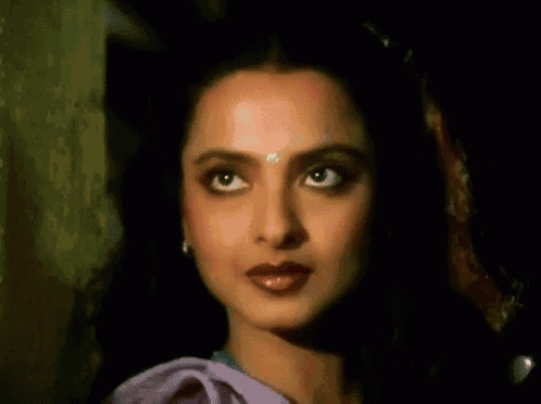 a close up of a woman 's face with a purple blouse and earrings .