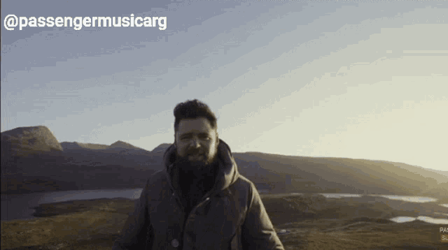 a man with a beard is standing in front of a mountain with passengermusicarg written on the top