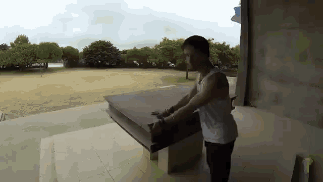 a man in a white tank top is standing in front of a table in a park