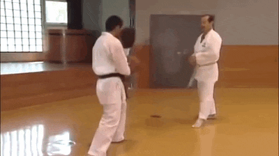 two men in white karate uniforms are standing on a karate mat in a gym .
