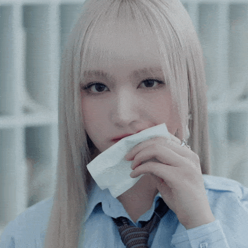 a girl with blonde hair and red lipstick is holding a piece of paper in front of her face