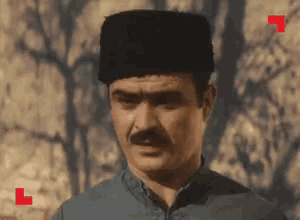 a man with a mustache wearing a black hat and a blue shirt .