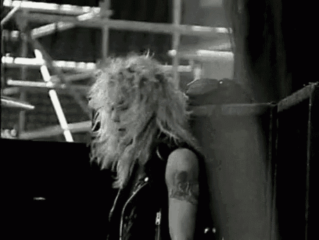 a black and white photo of a heavy metal artist standing next to a wall .