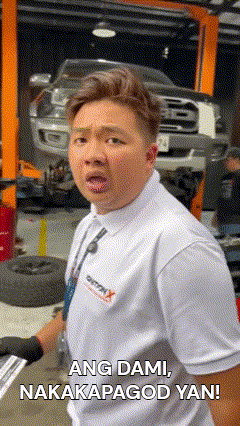 a man in a white shirt and tie is standing in front of a car on a lift in a garage .