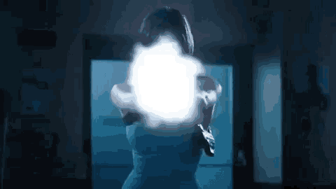 a woman is holding a gun in a dark room and shooting a light .