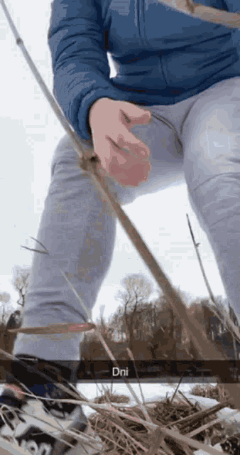 a person wearing a blue jacket and grey pants is holding a fishing rod and the word dni is on the bottom right