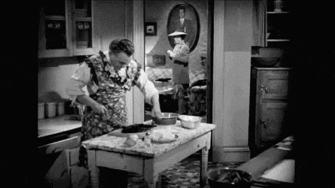 a black and white photo of a woman preparing food in a kitchen .
