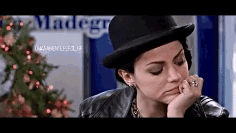 a woman wearing a hat and a leather jacket is sitting in front of a madegr sign