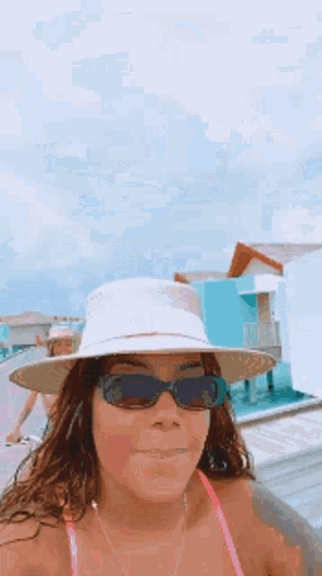 a woman wearing a hat and sunglasses is standing by a pool .