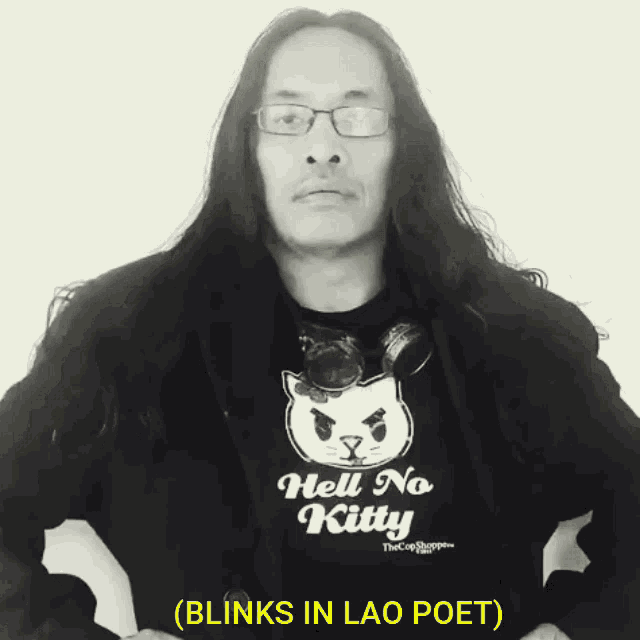 a man with long hair and glasses wears a shirt that says hell no kitty