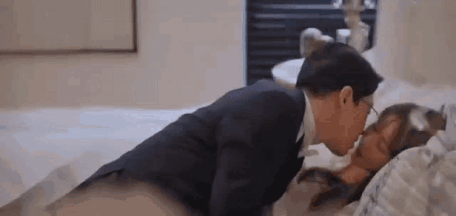 a man in a suit is kissing a woman on the forehead while laying on a bed .