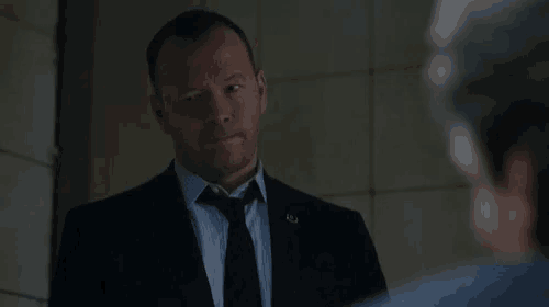 a man in a suit and tie is talking to another man in a room .