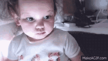 a baby girl is looking at the camera while sitting on a bed .