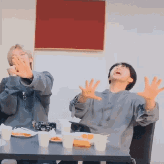 two people are sitting at a table with their hands in the air and making funny faces .