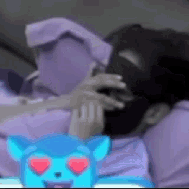 a blurry picture of a person laying down with a blue cat with hearts on its eyes .