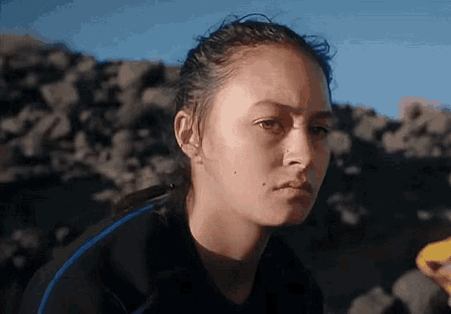 a woman in a wetsuit is sitting on a rocky beach .