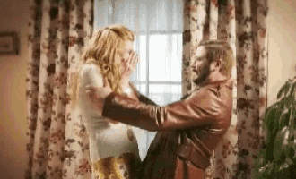 a man in a leather jacket is holding a woman in his arms in a living room .