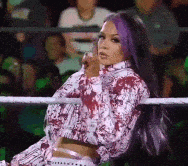 a woman with purple hair is sitting in a wrestling ring with a crowd watching .