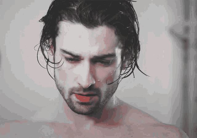 a man without a shirt is taking a shower and his hair is wet