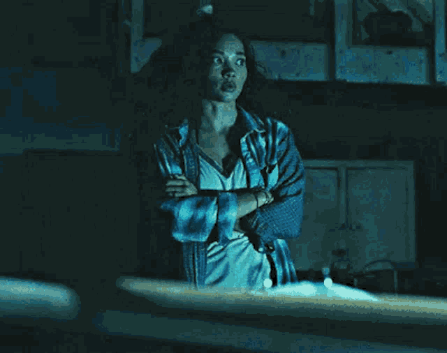 a woman with her arms crossed is standing in a dark room .