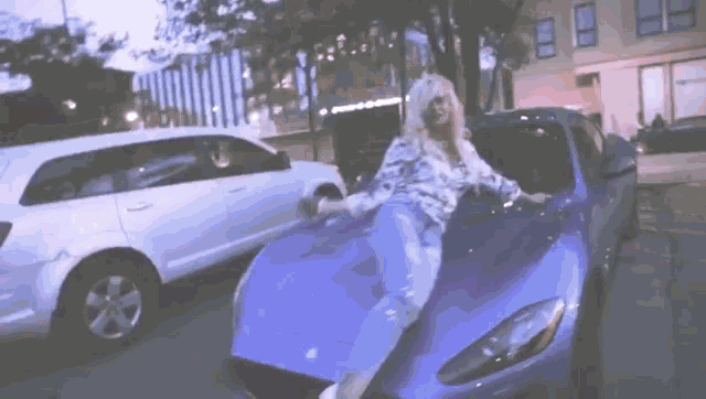a woman sits on the hood of a blue sports car