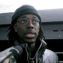 a man wearing a beanie and glasses is talking into a microphone